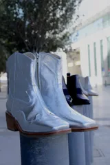 Botas plateadas de cuero con caña media, punta cuadrada, cierre lateral y diseño bordado estilo western.