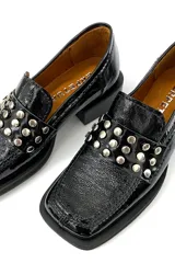Mocasín de cuero charol negro con detalle de apliques metálicos plateados en la parte delantera y taco bajo cuadrado.