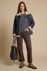 Campera tipo gamulán de corte oversize, color azul marino con interior y cuello de corderito en tono beige. Presenta detalles de costuras y bordes en cuero sintético color marrón, cierre frontal y mangas largas.