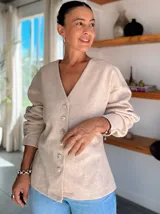 Chaqueta tipo bomber color beige, con cuello en V, cierre frontal con botones y mangas largas con diseño holgado. Confeccionada en tela suave de textura lisa.