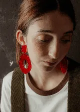 Aros colgantes con forma geométrica irregular, color rojo. El aro superior es pequeño y redondeado, mientras que el aro inferior es grande y con un agujero en el centro.