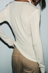 Camiseta de manga larga color crudo con cuello redondo y detalle de top halter superpuesto en el mismo tejido. Presenta un diseño de doble capa con caída drapeada en el frente.