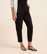 Pantalón de vestir femenino color marrón oscuro, de corte fluido y tiro medio/alto, con cintura elástica ajustable mediante cordón. Presenta bolsillos laterales y cierre frontal.