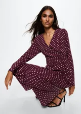 Mono largo de tejido fluido con estampado de lunares. Presenta cuello en pico, mangas largas acampanadas y un nudo ajustable en la cintura que entalla la silueta. Incluye forro interior.