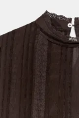 Blusa blanca de cuello alto con detalles de puntilla, manga corta abullonada y cierre posterior con botón.
