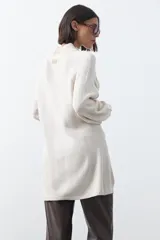 Vestido corto de punto en color beige, con cuello alto acanalado, mangas largas con puños ajustados y diseño holgado.