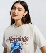 Remera de algodón color crema con cuello redondo y manga corta. Presenta un estampado frontal con el personaje Stitch sosteniendo una taza de café y la leyenda 'Coffee Mornings Club'.