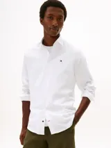 Camisa de corte regular de Tommy Hilfiger, confeccionada en sarga de algodón blanco, con cuello clásico, cierre frontal de botones y el característico logo bordado en el pecho.