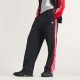 Pantalón Adidas Originals de corte holgado, confeccionado en tejido de malla color negro. Presenta las icónicas tres tiras laterales en color rojo y el logo del trébol bordado en la pierna.