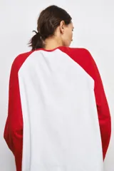 Camiseta de manga larga con diseño ranglan, cuerpo en color blanco y mangas en color rojo. Presenta cuello redondo y bajo recto.