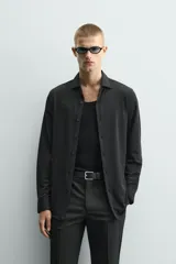 Camisa de manga larga color verde oscuro, con cuello italiano abierto y cierre frontal de botonadura. Presenta un calce ajustado (slim fit) y puños con botón.