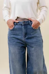 Jean de corte wide leg y tiro alto, confeccionado en denim rígido con un ligero efecto de desgaste. Presenta un diseño de calce relajado con pernera amplia, cintura marcada, bolsillos clásicos y cierre frontal con botón metálico.