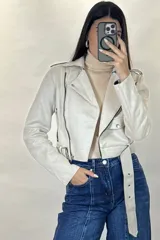 Chaqueta corta tipo biker confeccionada en gamuza color beige, con cierre frontal cruzado, solapas amplias, bolsillos con cierre y cinturón ajustable en la cintura.