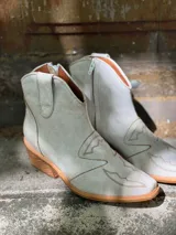 Botas cortas de cuero sintético color beige con detalles de costuras estilo western.