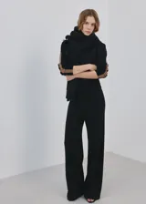 Pantalón de punto negro con diseño recto y holgado, con una franja lateral en tono marrón.