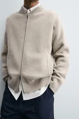 Chaqueta tipo bomber de punto en hilatura de lana, con cuello subido, manga larga, bolsillos de vivo en la cadera, acabados en rib y cierre frontal de cremallera.