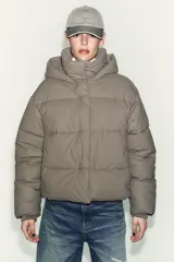 Campera puffer corta de tejido engomado resistente al viento, con aislamiento térmico. Presenta cuello subido con capucha, manga larga, bolsillos delanteros y bajo ajustable con stoppers laterales. Cierre frontal con cremallera termosellada y botones magnéticos.