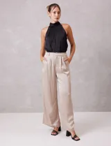 Pantalón palazzo de tiro alto confeccionado en tela satinada. Presenta una pretina delantera con pasadores, cierre y broche, mientras que la parte trasera cuenta con elástico para mayor comodidad. Incluye bolsillos verticales en el frente.