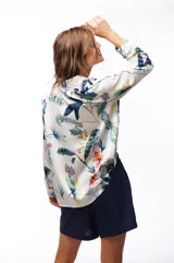 Camisa de manga larga con estampado floral en tonos azules, verdes, naranjas y amarillos sobre fondo blanco.