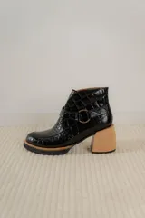 Bota corta de cuero vacuno con textura de reptil, color marrón oscuro. Cuenta con un taco cuadrado negro, suela de plataforma y una tira decorativa con hebilla metálica circular en el tobillo.