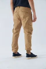 Pantalón cargo color beige, corte slim, con bolsillos laterales con botón, cierre con botón y puños en los tobillos.