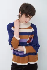 Polera de tejido de punto con diseño de rayas horizontales en tonos beige, marrón, gris y negro. Presenta cuello redondo y mangas largas con puños en contraste.