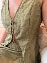 Conjunto de dos piezas color verde oliva con textura arrugada. Incluye un chaleco sin mangas con cierre frontal de lazos y una minifalda ajustada.