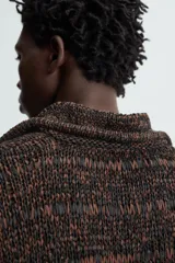 Polo de punto de calce relajado, color marrón oscuro jaspeado con negro. Presenta cuello solapa con abertura frontal en V y mangas cortas.