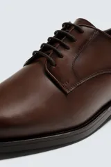 Zapato de vestir estilo Derby color marrón, fabricado en piel con horma redonda, cordones finos y suela con ligero tacón.