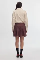 Camisa de tacto de seda color beige, entallada en la cintura, con cuello camisero, bolsillos frontales con solapa y bordados, y cordón decorativo en el cuello.