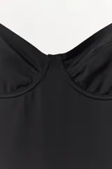 Vestido mini negro con escote corazón y aros integrados en el busto. Presenta tirantes finos ajustables y un diseño entallado con efecto reductor que estiliza la figura.