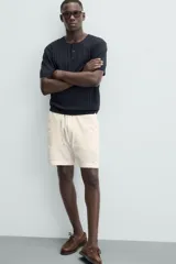 Bermuda de calce regular, color beige claro, confeccionada en tejido de mezcla de algodón con textura jacquard. Presenta cintura elástica ajustable con cordón, bolsillos frontales y un bolsillo trasero de vivo.