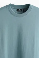 Remera de manga corta color verde, confeccionada en punto liviano, con cuello redondo ribeteado, hombros caídos, bajo recto y corte relajado.