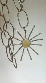 Collar con cadena de eslabones plateados y dije artesanal con forma de sol, con centro de nácar y rayos de alpaca.