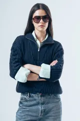 Sweater de punto grueso color azul marino, con cuello polo y cierre frontal parcial. Presenta un diseño de tejido trenzado en el centro y mangas largas con puños acanalados.