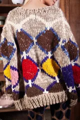 Sweater de lana tejido a mano con diseño de rombos multicolor en tonos tierra, rojo, amarillo y azul. Presenta un corte holgado, cuello redondo y puños acanalados.