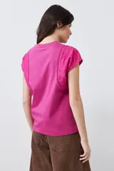 Remera fucsia de algodón con mangas cortas que presentan detalles de broderie y costuras decorativas.