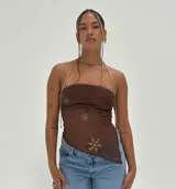 Top tipo bandeau/pañuelo marrón oscuro, confeccionado en tela transparente con bordados de cuentas doradas que forman patrones circulares y florales. Se sostiene con tirantes finos de cuentas plateadas que se anudan al cuello.