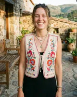 Chaleco de algodón color crudo con bordados florales en rojo, azul y amarillo. Tiene un cierre frontal con lazos.