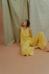 Mono largo de lino color amarillo, con escote en V, tirantes finos y detalles de costuras decorativas blancas en el escote y en los bajos de las piernas anchas.