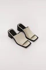 Sandalia de cuero vacuno color marrón oscuro, con faja ancha y punta cuadrada. Presenta talón abierto y taco bajo y grueso.