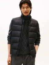 Chaleco acolchado negro con cuello alto y cierre frontal de cremallera. Presenta un pequeño logo bordado de Tommy Hilfiger en el pecho.