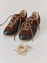 Championes de cuero con diseño combinado en color marrón y negro. Presentan una estructura de gamuza marrón con refuerzos de cuero liso negro en la puntera y laterales, cordones bicolores y suela de goma.