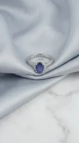 Anillo de plata 925 con piedra central ovalada en color azul zafiro, rodeada de pequeñas circonias y pavé de circonias en los hombros.