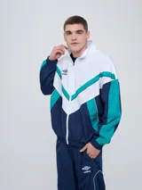 Campera deportiva Umbro modelo Beat, confeccionada en nylon ligero con diseño de bloques de color en blanco, azul marino y verde azulado. Presenta cierre frontal, cuello alto y elásticos en puños y cintura.