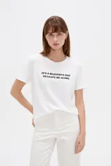 Remera de algodón blanca, de manga corta y cuello redondo, con estampado frontal de texto en color negro.