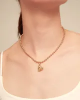 Dije de corazón dorado con inscripción de la marca Uno de 50.