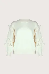 Suéter de punto color blanco, con cuello redondo, mangas largas abullonadas y detalle de volantes en los hombros y antebrazos.