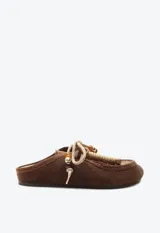 Zueco de gamuza marrón, estilo slip-on, con cordones frontales decorativos, abalorios y suela plana.