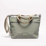 Bandolera de material sintético color verde salvia, con dos cierres frontales horizontales y un parche rectangular en la parte inferior central. Posee asas cortas de tela color beige y una correa larga ajustable del mismo color. Incluye un accesorio colgante de cordones trenzados en verde claro y un dije de madera.